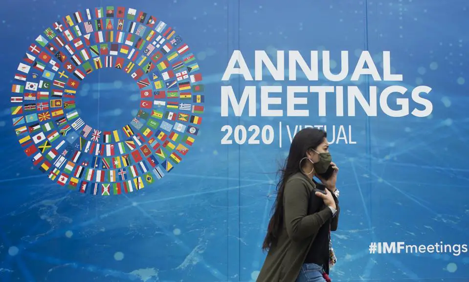 Una mujer pasa por delante de un cartel promocional de las reuniones anuales virtuales de 2020 en las afueras del Fondo Monetario Internacional en su sede de Washington, DC, el 13 de octubre de 2020.