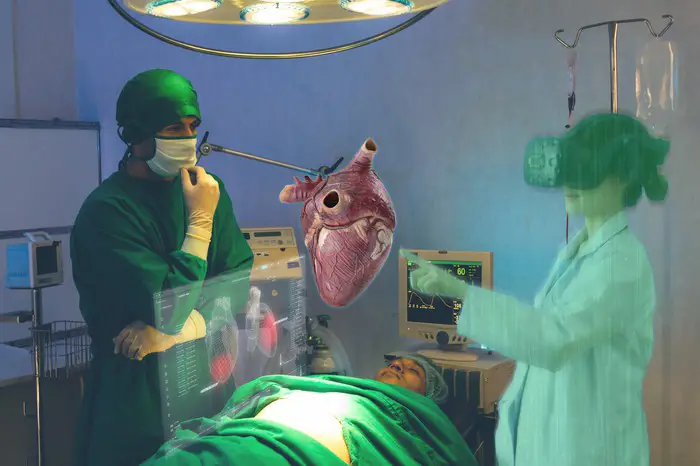 Dos doctores en la sala de operaciones con un corazón virtual flotando sobre el paciente en la mesa.