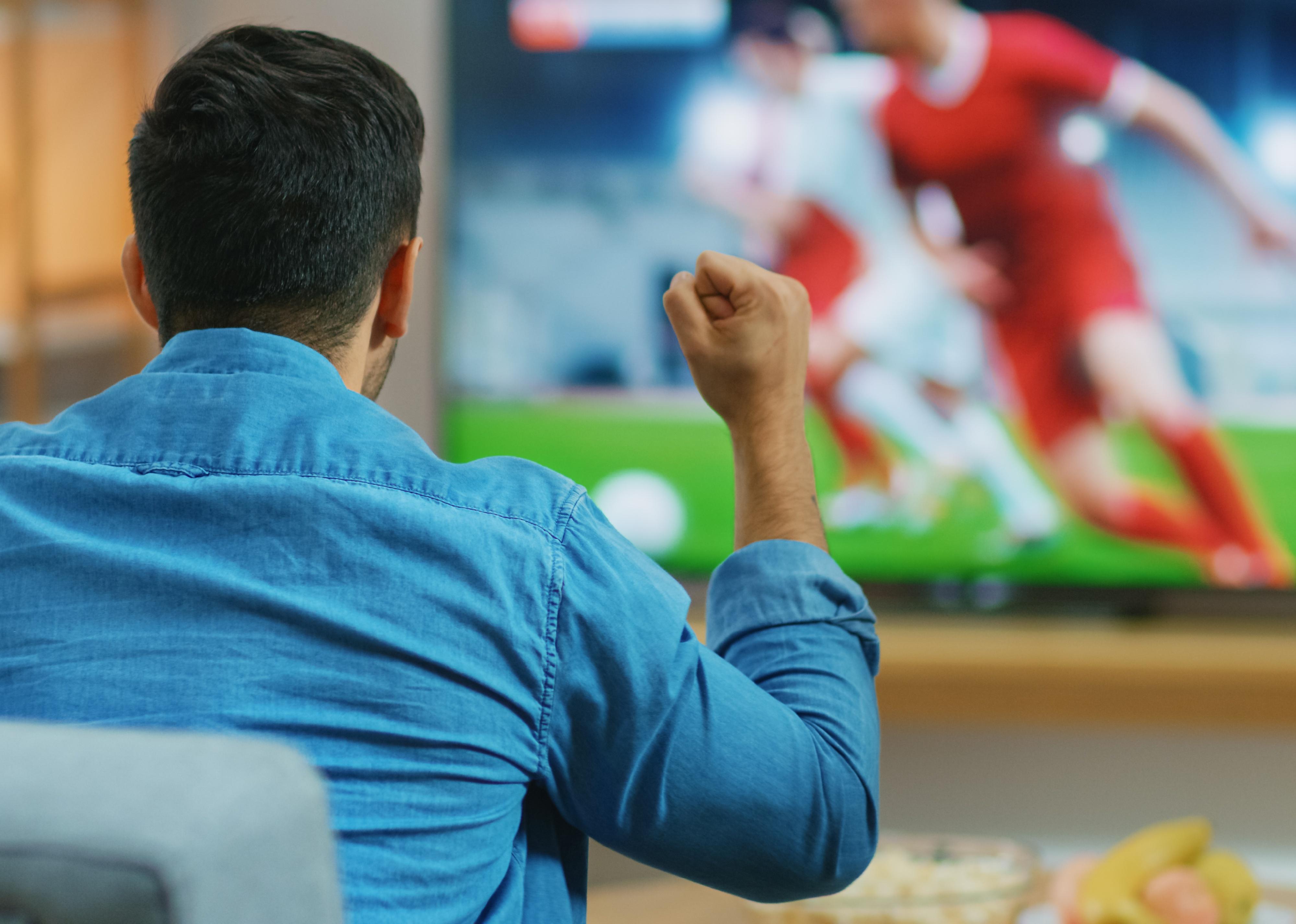El hombre ve un partido de fútbol en la televisión.