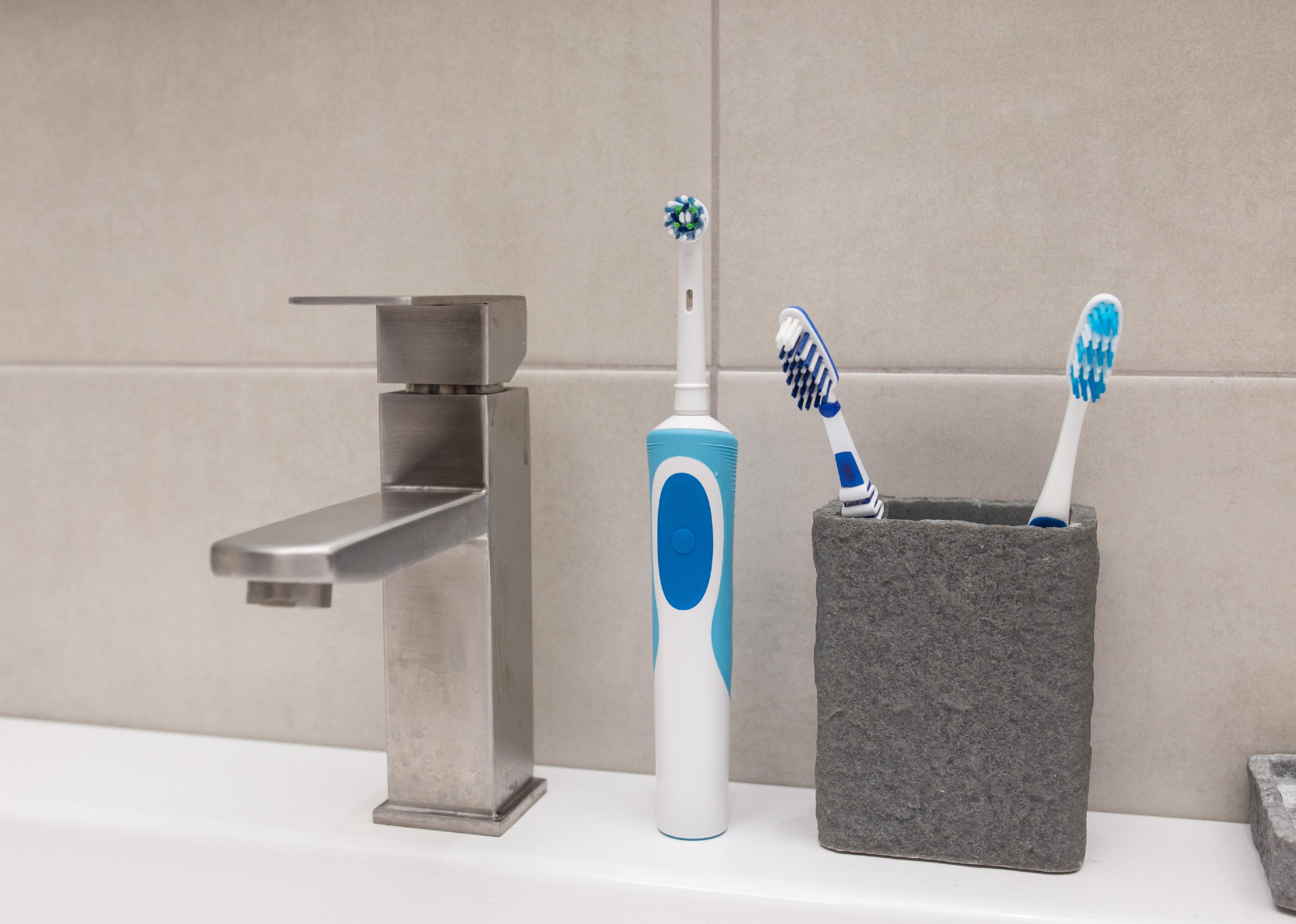 Un cepillo de dientes eléctrico y un cepillo de dientes viejo cerca del lavabo.
